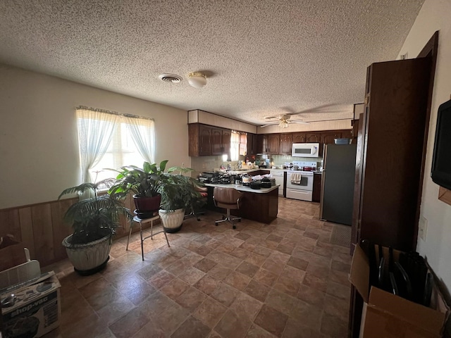 kitchen featuring light countertops, visible vents, dark brown cabinets, white appliances, and a peninsula