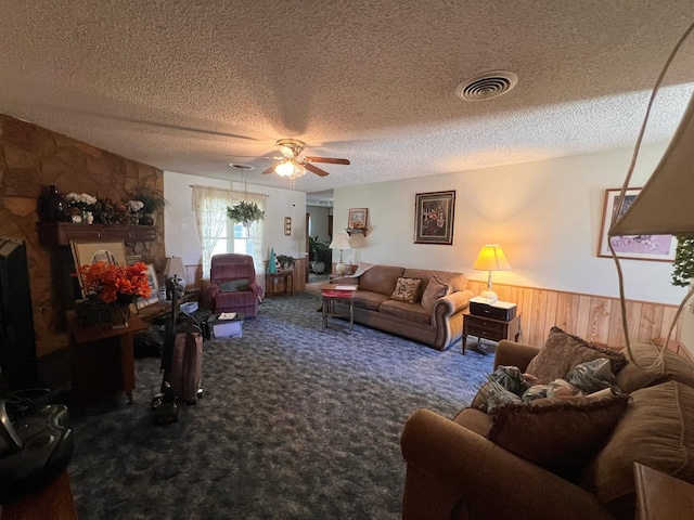 carpeted living room with a wainscoted wall, visible vents, a ceiling fan, wooden walls, and a textured ceiling