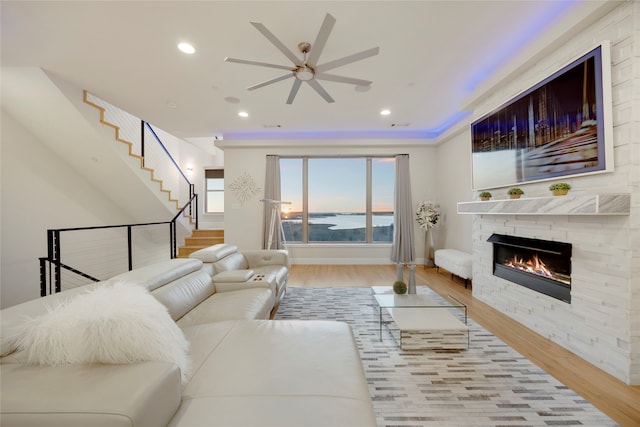 living room featuring stairs, a stone fireplace, recessed lighting, wood finished floors, and a ceiling fan