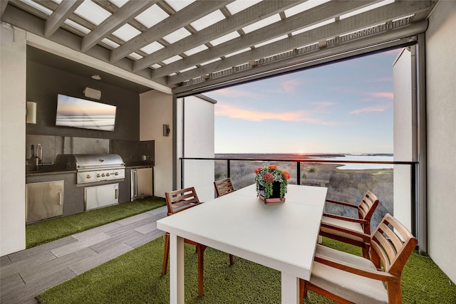 exterior space featuring a water view, outdoor dining space, an outdoor kitchen, a grill, and a sink