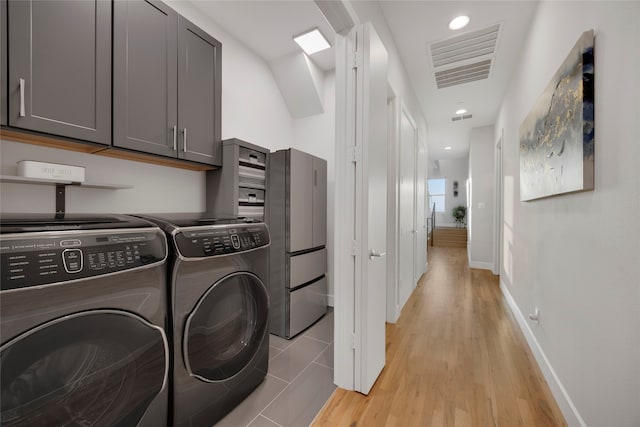 washroom with visible vents, light wood-style flooring, cabinet space, baseboards, and washing machine and clothes dryer