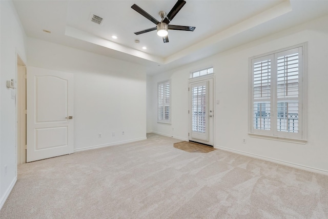 empty room featuring carpet floors, a raised ceiling, visible vents, and baseboards