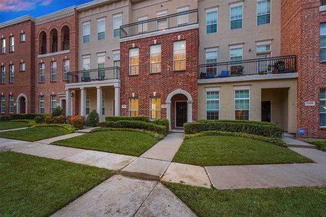 townhome / multi-family property with brick siding, a front yard, and stucco siding