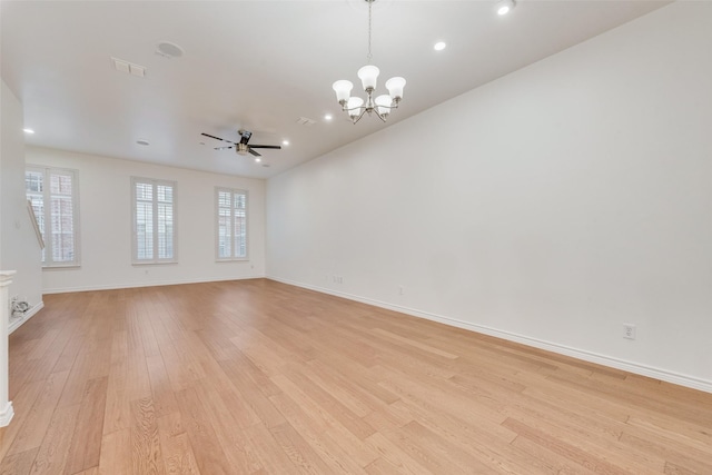 empty room featuring ceiling fan with notable chandelier, light wood finished floors, visible vents, and baseboards