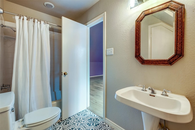 bathroom with a textured wall, a sink, toilet, and shower / tub combo with curtain