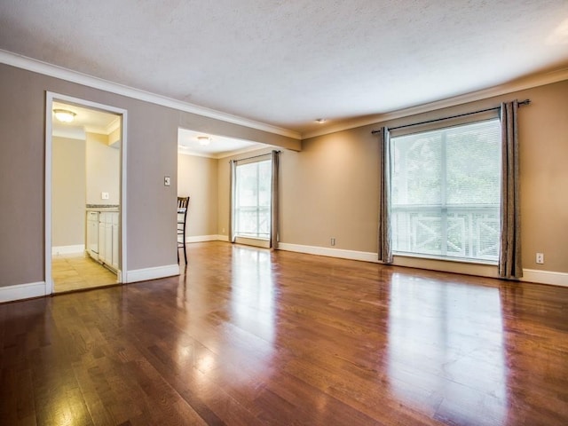 spare room featuring crown molding, baseboards, and wood finished floors