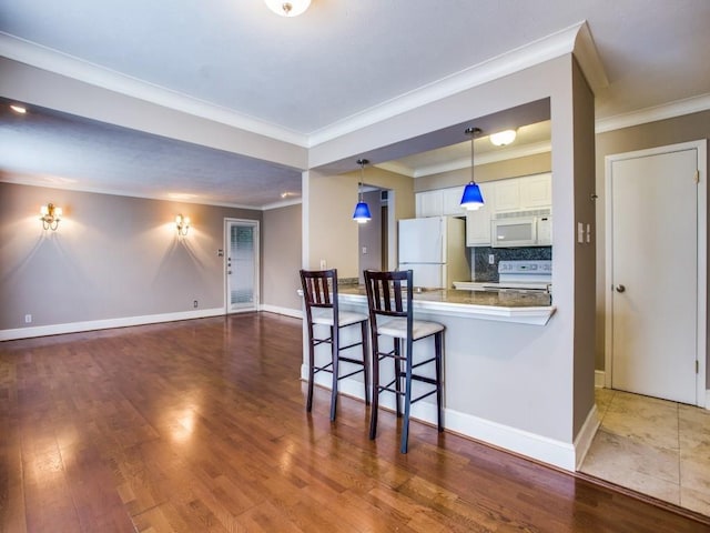 kitchen with backsplash, white cabinets, wood finished floors, white appliances, and a peninsula