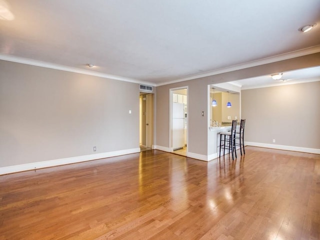 empty room with ornamental molding, wood finished floors, visible vents, and baseboards