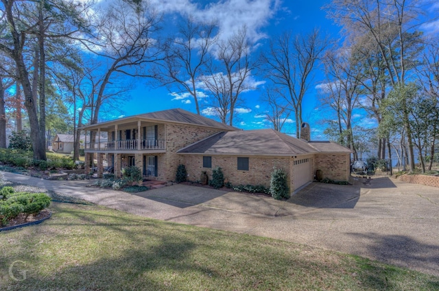 view of side of home with aphalt driveway, brick siding, a chimney, a balcony, and a garage