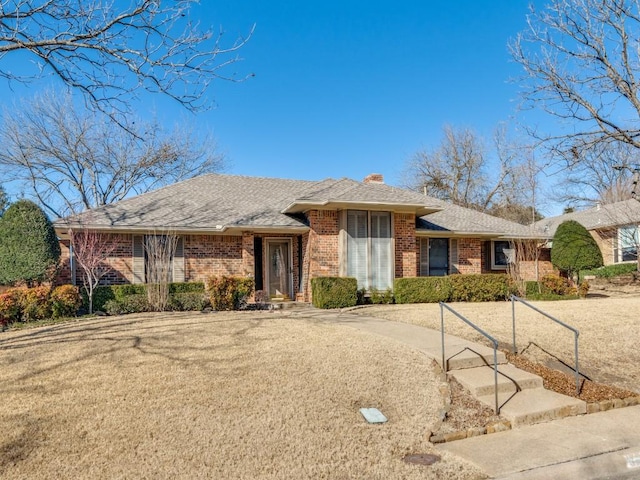 single story home with a shingled roof, brick siding, and a chimney