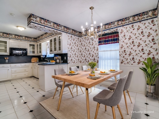 dining area featuring light tile patterned flooring, a wainscoted wall, an inviting chandelier, and wallpapered walls