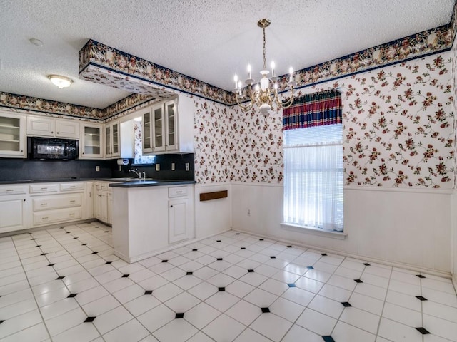 kitchen featuring black microwave, a wainscoted wall, a textured ceiling, and wallpapered walls