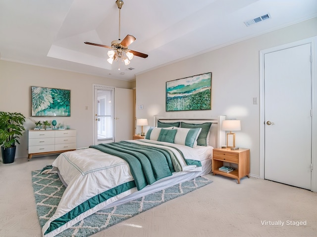 carpeted bedroom with ornamental molding, a tray ceiling, visible vents, and ceiling fan