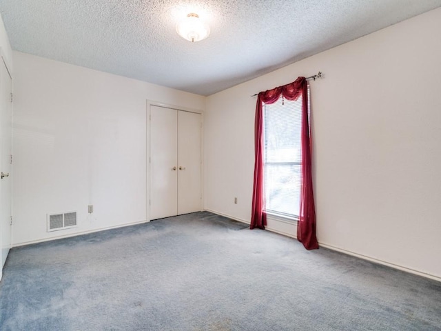 empty room featuring carpet, visible vents, and a textured ceiling