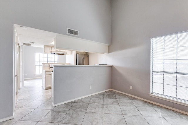 empty room featuring a high ceiling, light tile patterned floors, baseboards, and visible vents