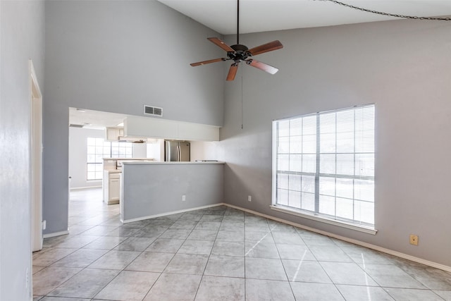 unfurnished living room with baseboards, visible vents, light tile patterned flooring, ceiling fan, and a towering ceiling