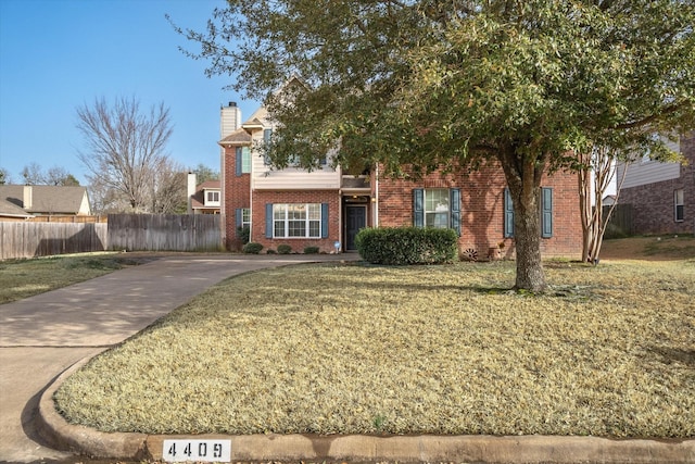 view of front of house featuring a chimney, fence, a front lawn, and brick siding