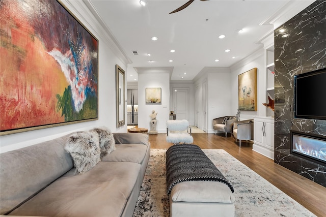 living area with recessed lighting, a premium fireplace, wood finished floors, visible vents, and ornamental molding