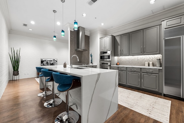 kitchen featuring visible vents, wall chimney exhaust hood, appliances with stainless steel finishes, gray cabinetry, and a sink