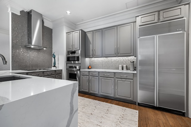 kitchen with wall chimney range hood, stainless steel appliances, a sink, and gray cabinetry