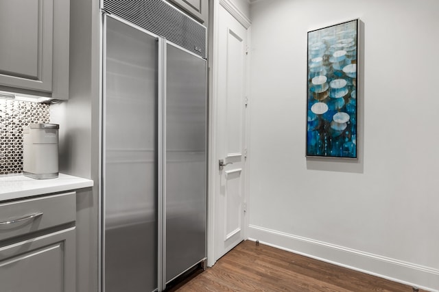 kitchen with gray cabinetry, dark wood-style flooring, built in refrigerator, light countertops, and backsplash