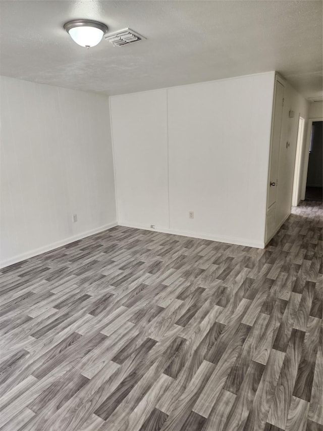 empty room featuring a textured ceiling, visible vents, and wood finished floors