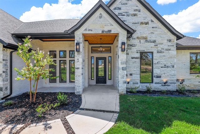 doorway to property featuring stone siding, roof with shingles, covered porch, and brick siding