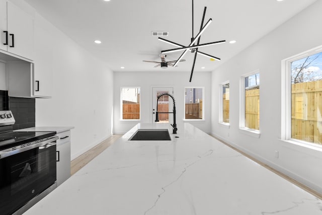 kitchen with light stone counters, recessed lighting, visible vents, electric range, and a sink