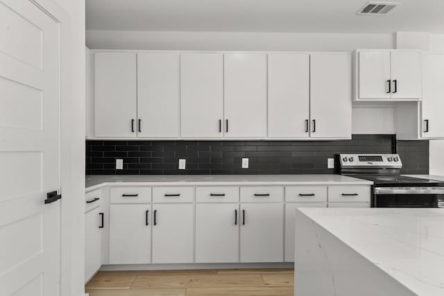 kitchen featuring light wood finished floors, stainless steel electric stove, visible vents, decorative backsplash, and white cabinetry