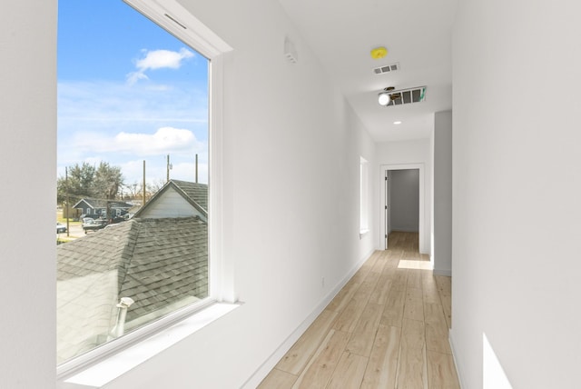 hall featuring light wood-style floors, visible vents, and baseboards