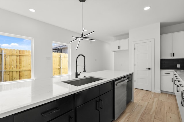 kitchen with tasteful backsplash, white cabinets, a sink, and stainless steel dishwasher