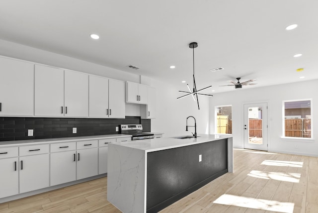 kitchen with tasteful backsplash, light wood-style flooring, a kitchen island with sink, stainless steel electric range, and a sink