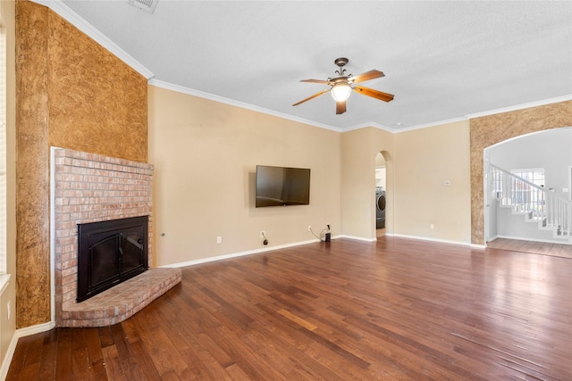 unfurnished living room featuring arched walkways, ceiling fan, a brick fireplace, wood finished floors, and washer / clothes dryer