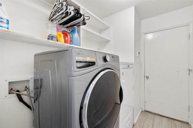 clothes washing area with washer and clothes dryer, light wood-style floors, and a textured ceiling