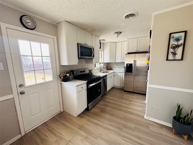 kitchen featuring light wood-style flooring, appliances with stainless steel finishes, light countertops, white cabinetry, and a sink