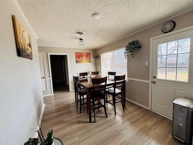 dining area featuring baseboards, visible vents, ornamental molding, a textured ceiling, and light wood-style floors