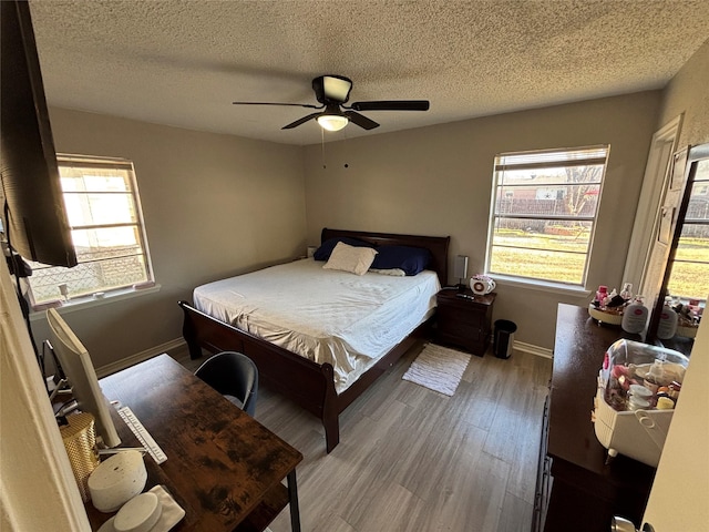 bedroom featuring multiple windows, wood finished floors, a ceiling fan, and baseboards