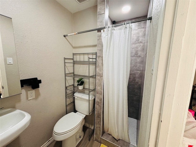 bathroom featuring tiled shower, a sink, toilet, and baseboards