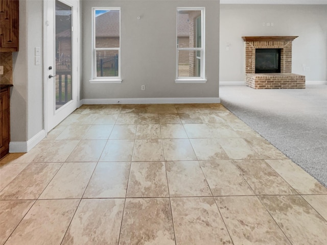 unfurnished living room featuring a brick fireplace, light carpet, baseboards, and light tile patterned floors