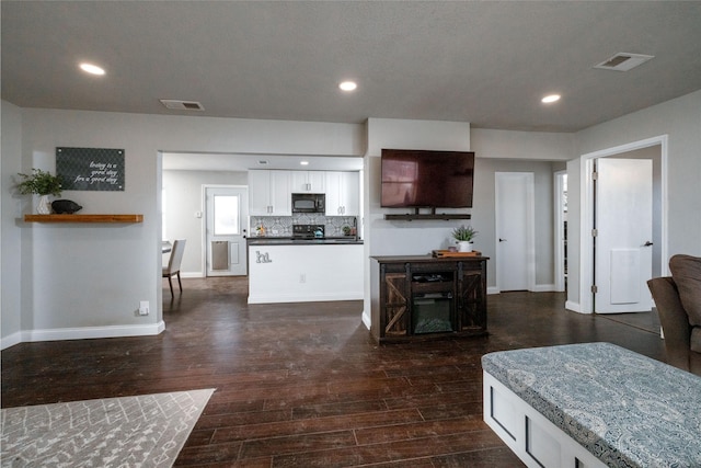 kitchen with tasteful backsplash, visible vents, dark wood-type flooring, white cabinetry, and black microwave