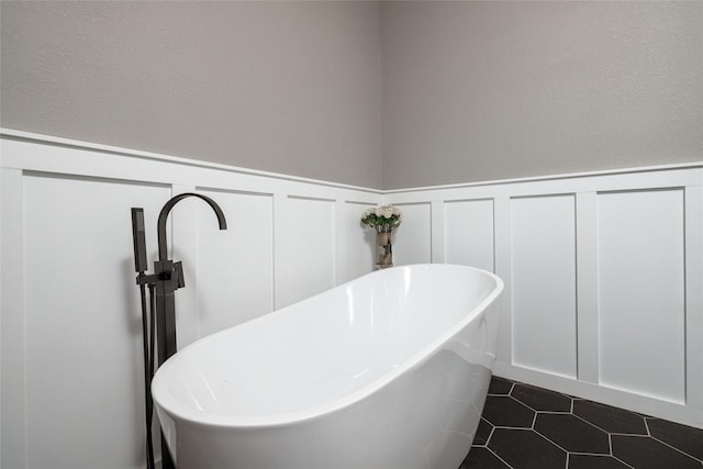 full bathroom featuring a soaking tub, wainscoting, tile patterned flooring, and a decorative wall