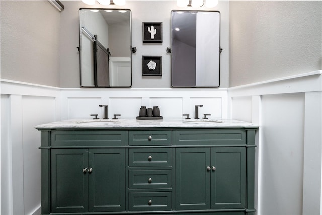 full bath featuring double vanity, wainscoting, a sink, and a decorative wall