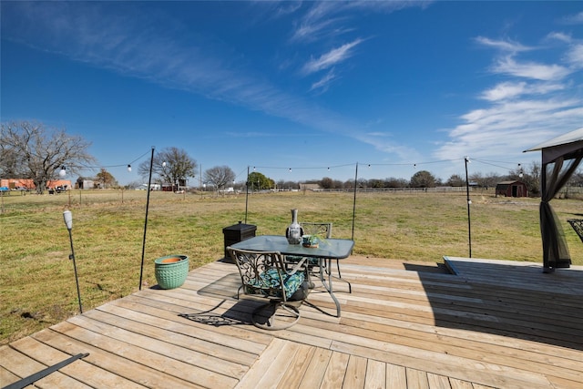 wooden terrace featuring outdoor dining area, a lawn, and an outbuilding