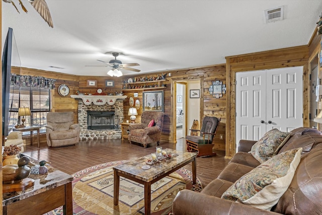 living room featuring visible vents, a ceiling fan, wood walls, a stone fireplace, and wood finished floors