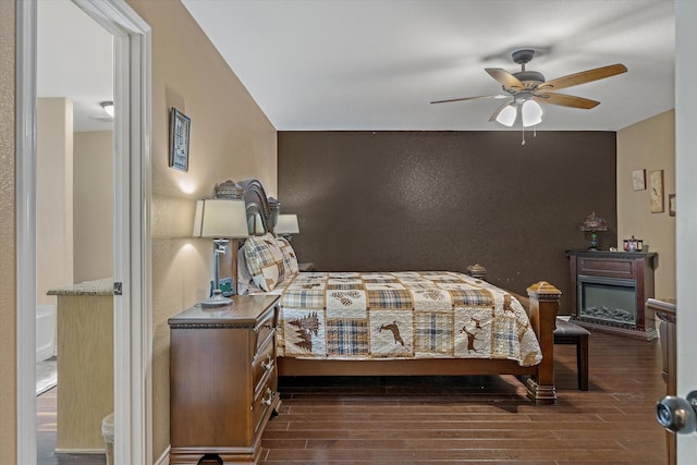 bedroom featuring ceiling fan, wood finished floors, and a glass covered fireplace