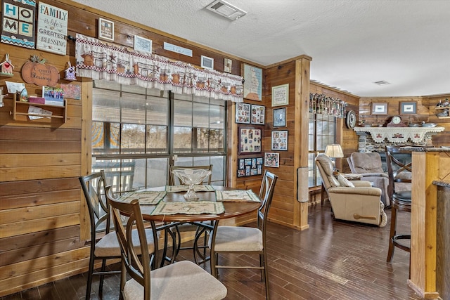 dining room with a textured ceiling, wood walls, wood finished floors, and visible vents