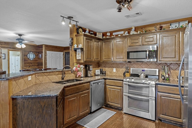 kitchen with stainless steel appliances, visible vents, dark wood-type flooring, a sink, and a peninsula