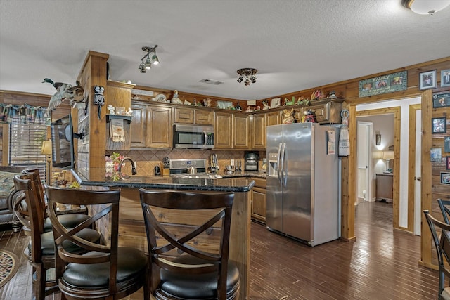 kitchen featuring visible vents, appliances with stainless steel finishes, brown cabinets, dark wood-style flooring, and a peninsula