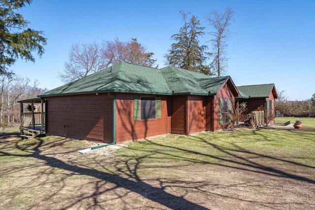 view of side of property featuring a shingled roof and a yard