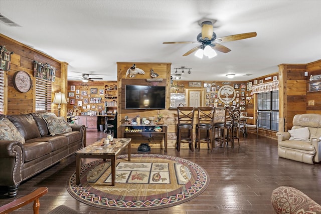 living area featuring visible vents, a ceiling fan, hardwood / wood-style floors, a bar, and wood walls